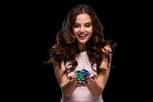 Sexy woman in a chic gently pink dress holding colored poker chips on a black background. Woman winning. Casino. Poker. Victory. Luck