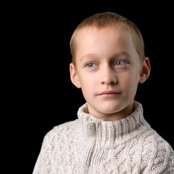 Close up portrait of a cute teenager. Handsome stylish boy in gray knitted jumper looking at camera. Teenage child posing in studio on black background
