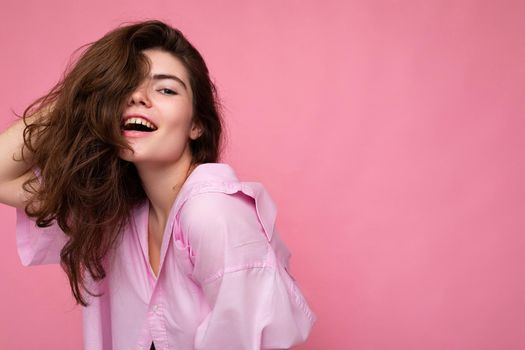 Portrait of beautiful happy sexy positive young curly brunette woman wearing pink shirt and grey hat isolated on pink background with copy space.