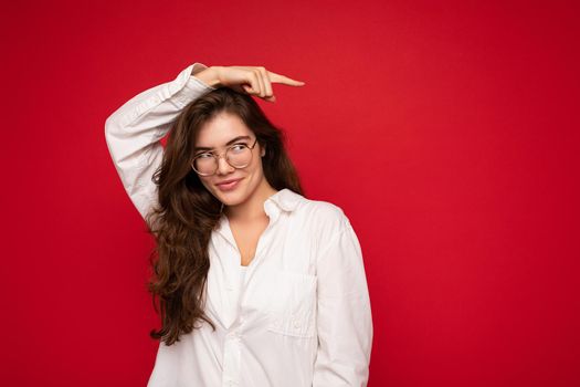 Beautiful young happy joyful funny curly brunette woman wearing white shirt and optical glasses isolated on red background with copy space.