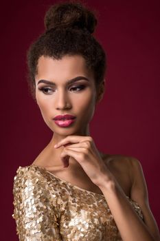 Fashion young African woman with make-up, in sexy gold dress. Model on a claret background in the studio