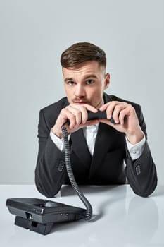 A young man in a black suit dials the phone number while sitting in the office. Manager looking at the camera and talking on the phone