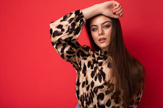 Fashion photo of young beautiful fashionable sexy brunette woman wearing stylish leopard blouse isolated on red background with empty space.