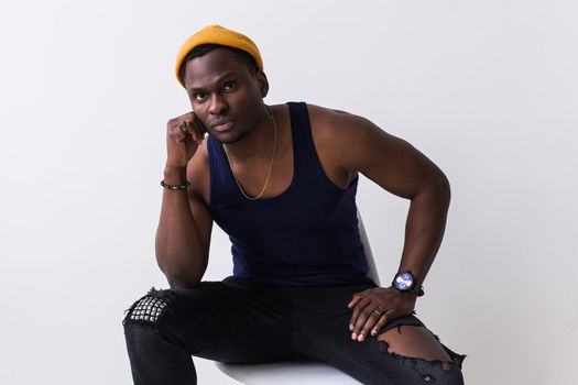 Portrait of sexy trendy african man sitting on a chair on white background. Youth concept
