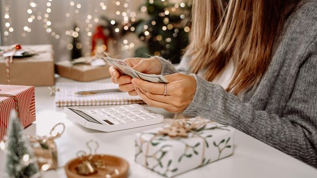 Girl counting US Dollar bills, using calculator, and writing expenses. Woman doing budget, estimating money balance for shopping spree. Female accountant paying taxes. Girl counting Christmas gifts.