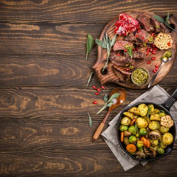 Meat steak with fried potatoes with vegetables and herbs on wooden cutting board. Healthy holiday food concept with copy space. Top view.