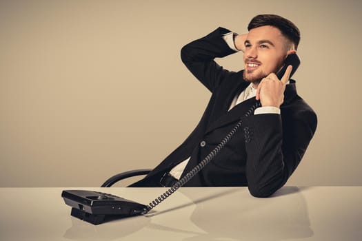 A young man in a black suit dials the phone number while sitting in the office. Manager talking on the phone