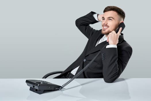 A young man in a black suit dials the phone number while sitting in the office. Manager talking on the phone