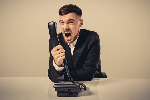 A young man in a black suit dials the phone number while sitting in the office. Manager talking on the phone. Man emotionally shouts