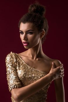 Fashion young African woman with makeup, in sexy gold dress. Model on a red background in the studio