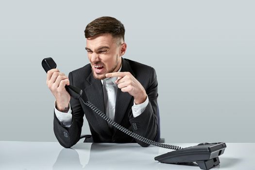 A young man in a black suit dials the phone number while sitting in the office. Manager talking on the phone. Man emotionally shouts