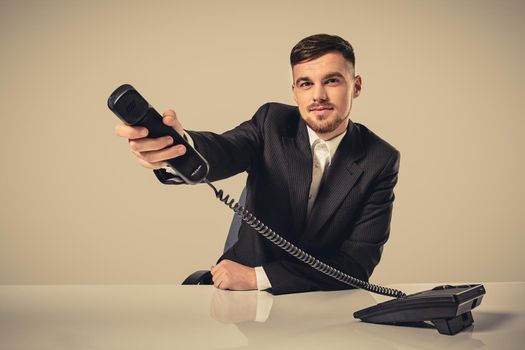 Portrait of attractive businessman holding telephone in his hand. This call is for you concept. A young man in a black suit dials the phone number while sitting in the office