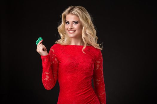 Young beautiful blond woman in a red dress with poker chips over black. Poker