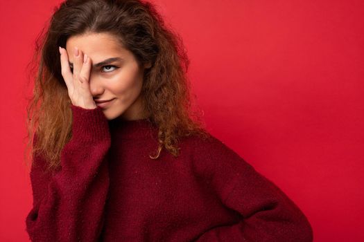 Young attractive curly brunette female person with sincere emotions poising isolated on background wall with copy space wearing casual dark red sweater. wtf concept.