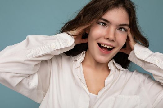 Beautiful funny amusing joyful cute nice adorable tender young curly brunette woman wearing white shirt isolated on blue background with copy space.