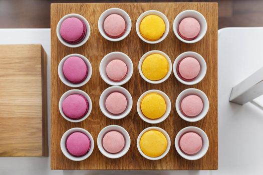 Top view of colourful macaroons served in cups arranged in even square shape on wooden stand