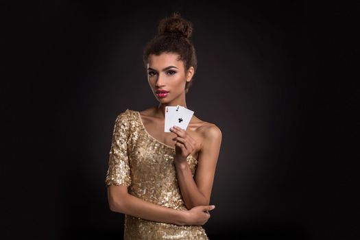 Woman winning - Young woman in a classy gold dress holding two aces, a poker of aces card combination. Studio shot on black background