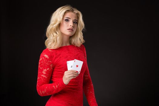 Young beautiful emotional woman with cards in hands on a black background in the studio. Portrait of a beautiful blonde in a red dress. Poker