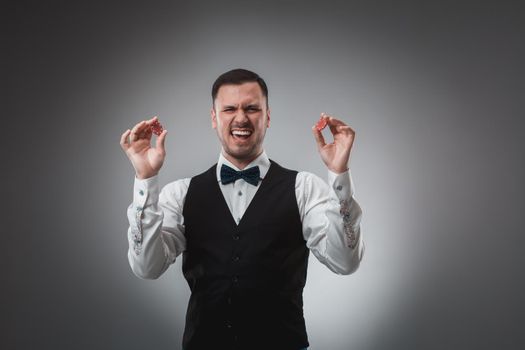 A man holding up red poker chips. Man in shirt and butterfly in studio on gray background. Poker