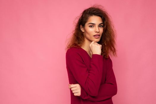 Photo of young european thoughtful charming cute brunette curly woman with sincere emotions wearing trendy pink sweater isolated over pink background with free space.