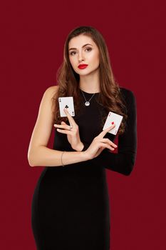 Beautiful caucasian woman in black dress with poker cards gambling in casino. Studio shot on red background. Poker. Two Aces in Hand