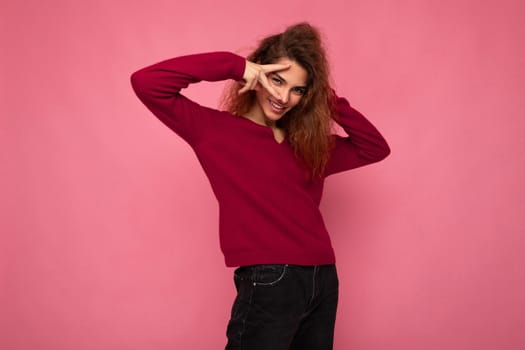 Portrait of young positive happy joyful beautiful brunette curly woman with sincere emotions wearing trendy pink pullover isolated on pink background with copy space.