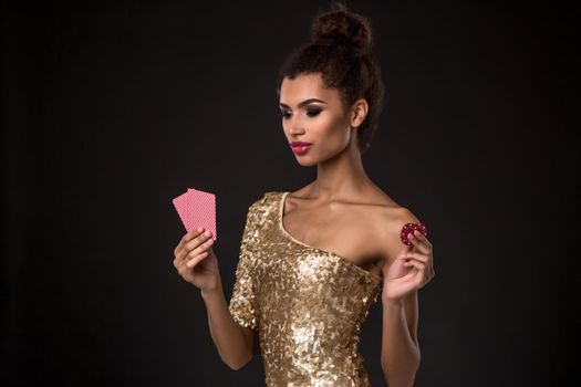 Woman winning - Young woman in a classy gold dress holding two cards and two red chips, a poker of aces card combination. Studio shot on black background