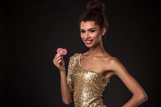 Woman winning - Young woman in a classy gold dress holding two red chips, a poker of aces card combination. Studio shot on black background