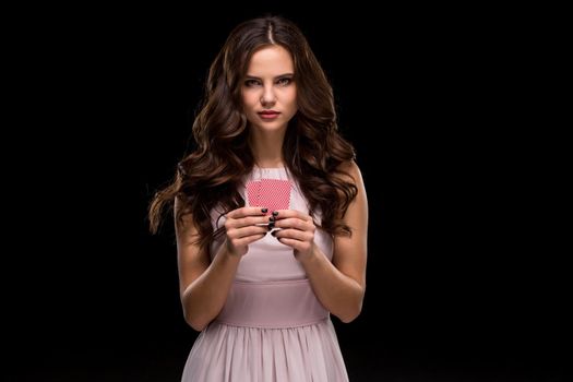 Beautiful confident woman in a sexy dress showing poker cards, looking at camera with copy place. Studio shot on black background. Casino