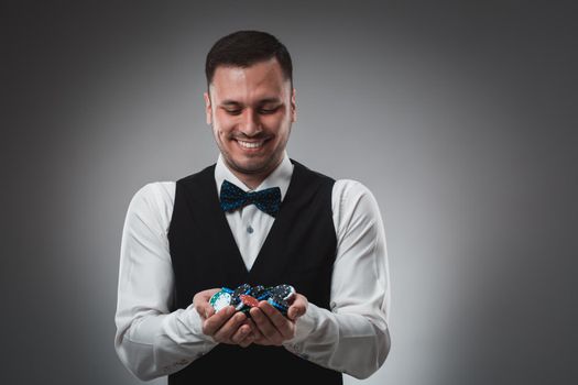 A man holding up poker chips. Man in shirt and butterfly in studio on gray background. Poker