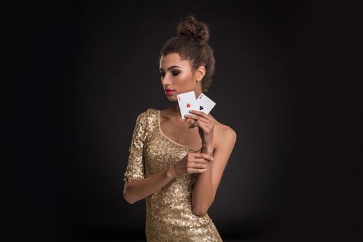 Woman winning - Young woman in a classy gold dress holding two aces, a poker of aces card combination. Studio shot on black background
