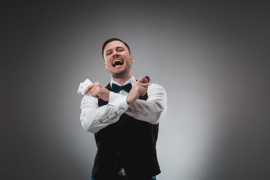 Young man in shirt and waistcoat shows his cards and holds poker chips in his hands, studio shot. Poker. Emotions