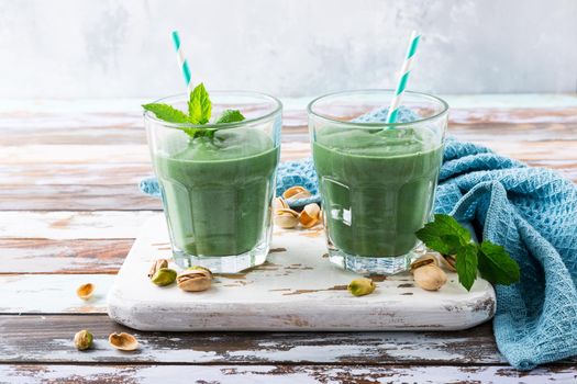 Two glasses of healthy green smoothie with mint, pistachios and spirulina on old wooden background. Detox, diet, healthy, vegetarian food concept with copy space.