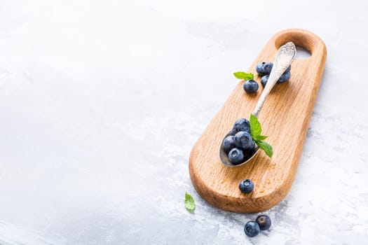 Fresh blueberries in vintage spoon on wooden cutting board. Healthy eating and nutrition concept with copy space.