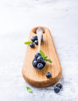 Fresh blueberries in vintage spoon on wooden cutting board. Healthy eating and nutrition concept with copy space.