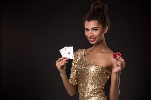 Woman winning - Young woman in a classy gold dress holding two aces and two red chips, a poker of aces card combination. Studio shot on black background