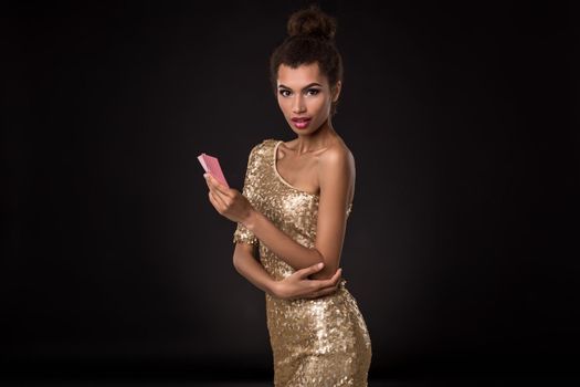 Woman winning - Young woman in a classy gold dress holding two cards, a poker of aces card combination. Studio shot on black background. Emotions