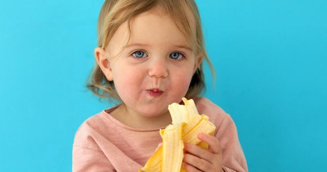 Funny Portrait of a young girl eating banana on a blue studio background