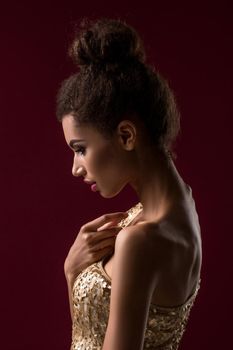 Fashion young African woman with make-up, in sexy gold dress. Model on a claret background in the studio. A woman is half a turn