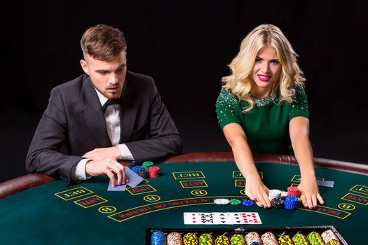 couple playing poker at the green table. The blonde girl and a guy in a suit. all-in bets chips