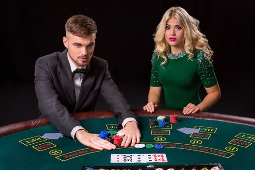 couple playing poker at the green table. The blonde girl and a guy in a suit. all-in bets chips