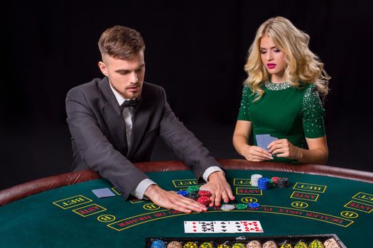 couple playing poker at the green table. The blonde girl and a guy in a suit. all-in bets chips