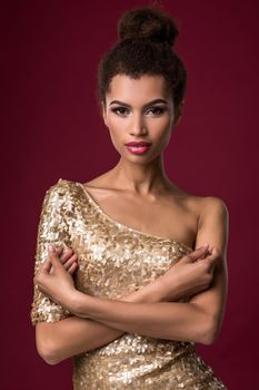 Fashion young African woman with makeup, in short sexy gold dress. Model on a red background in the studio