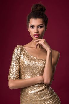 Fashion young African woman with makeup, in short sexy gold dress. Model on a red background in the studio