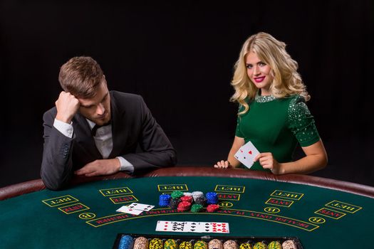 couple playing poker at the green table. The blonde girl and a guy in a suit. happy win, two aces