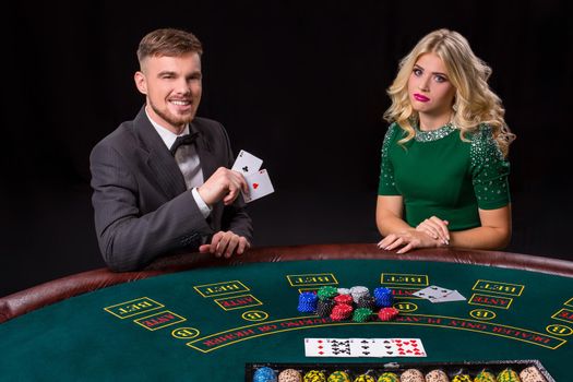 couple playing poker at the green table. The blonde girl and a guy in a suit. happy win, two aces