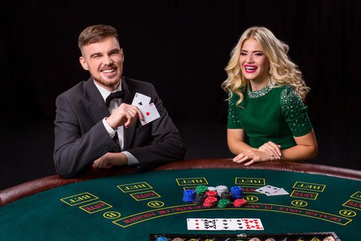 couple playing poker at the green table. The blonde girl and a guy in a suit. happy win, two aces