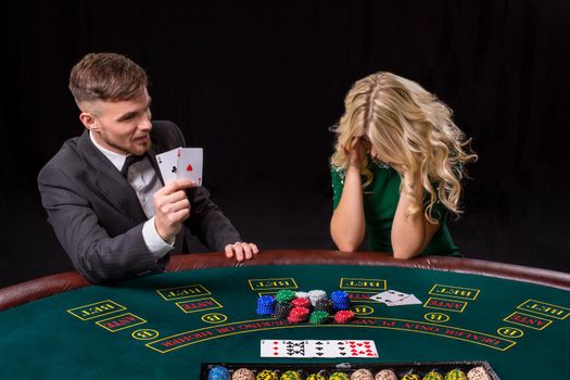 couple playing poker at the green table. The blonde girl and a guy in a suit. happy win, two aces