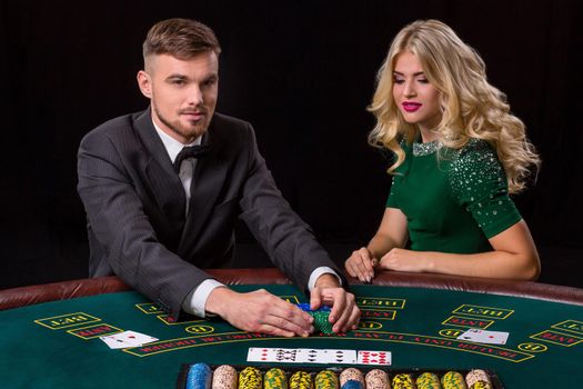 couple playing poker at the green table. The blonde girl and a guy in a suit. happy win