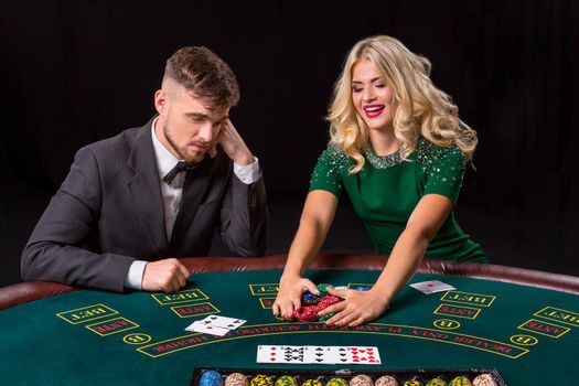 couple playing poker at the green table. The blonde girl and a guy in a suit. happy win